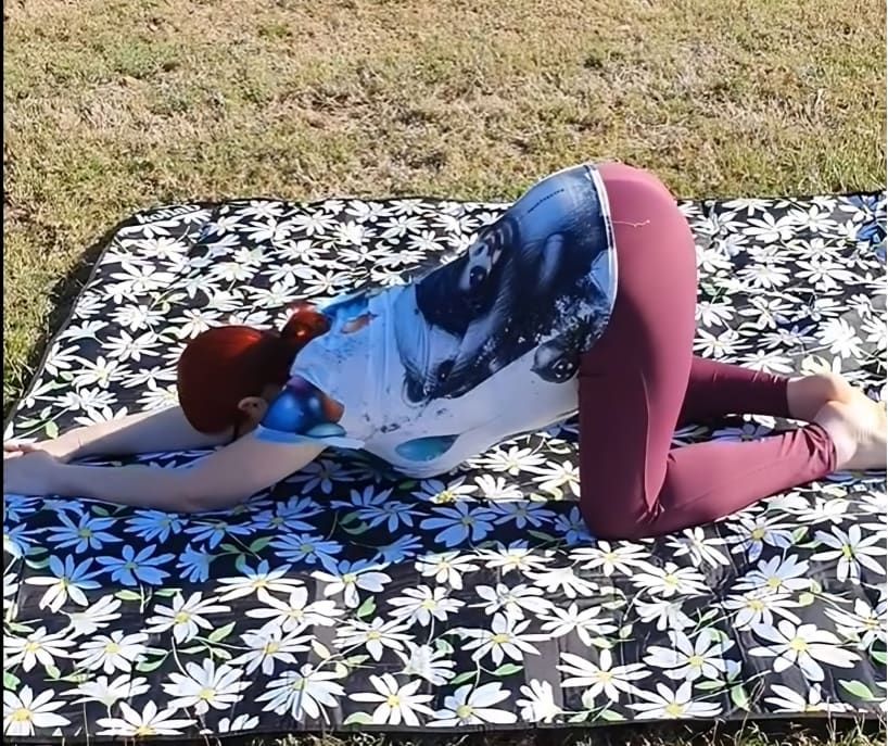 A Woman is Stretching on a Blanket With Daisies on It — Anderson Family Chiropractic Health Centre in Mount Pleasant, QLD