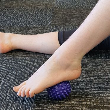 A Person is Laying on the Floor With Their Foot on a Purple Massage Ball — Anderson Family Chiropractic Health Centre in Mount Pleasant, QLD
