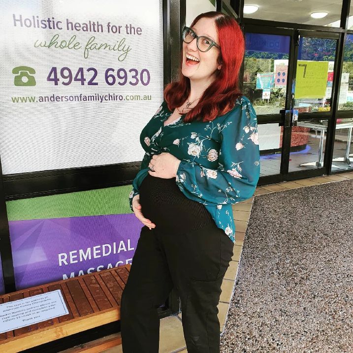A Pregnant Woman is Standing in Front of a Sign — Anderson Family Chiropractic Health Centre in Mount Pleasant, QLD