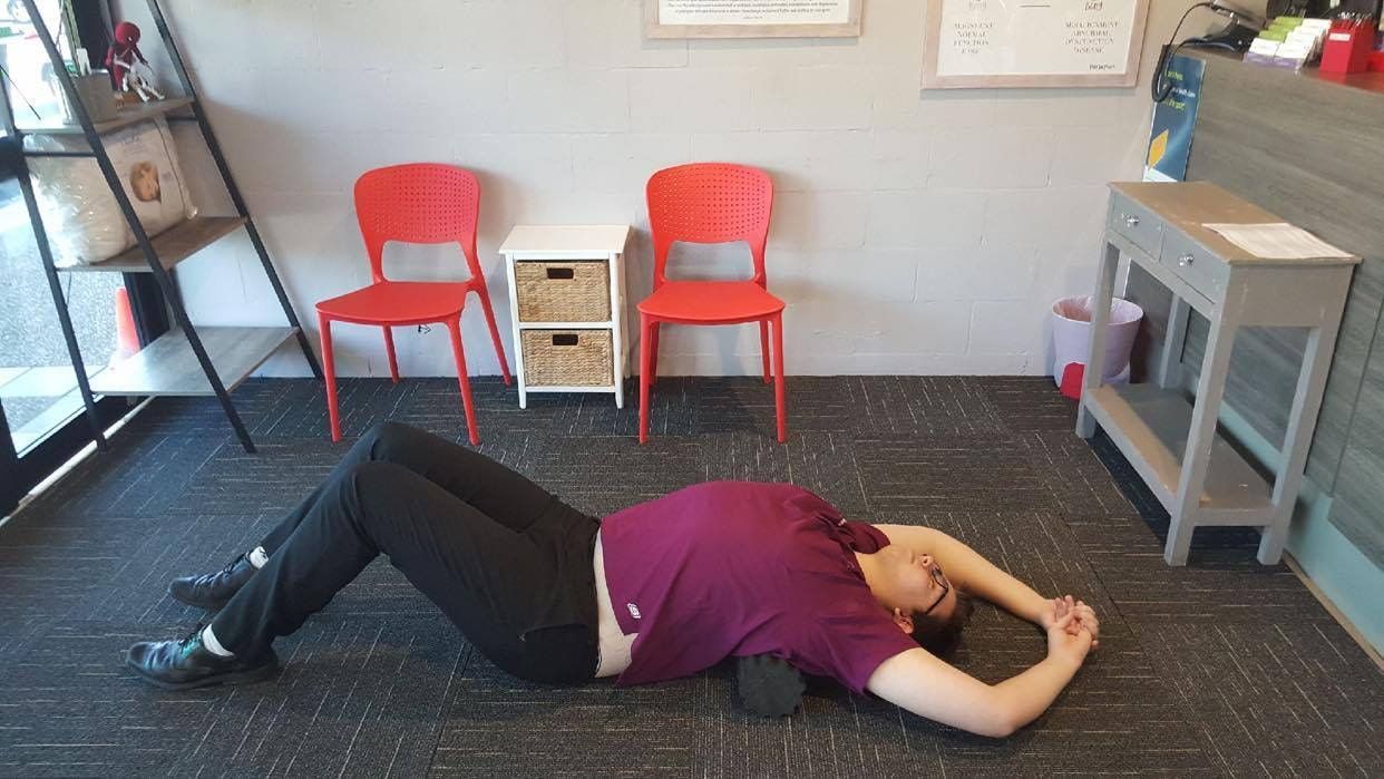 A Woman is Laying on the Floor With a Foam Roller on Her Back — Anderson Family Chiropractic Health Centre in Mount Pleasant, QLD