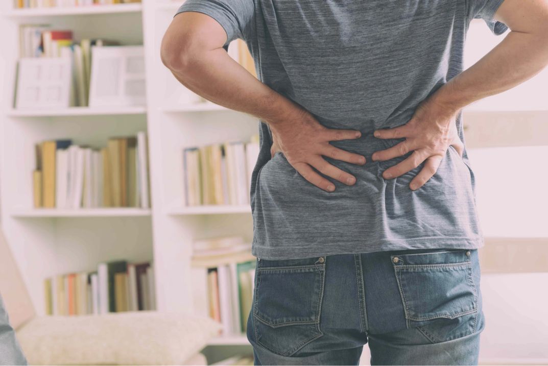 A Man is Holding His Back in Pain — Anderson Family Chiropractic Health Centre in Mount Pleasant, QLD