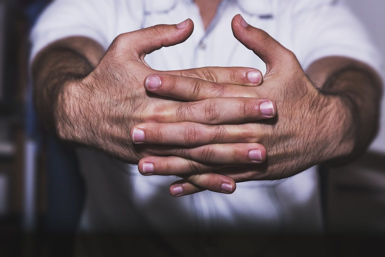 A Man is Sitting With His Hands Folded in Front of Him — Anderson Family Chiropractic Health Centre in Mount Pleasant, QLD