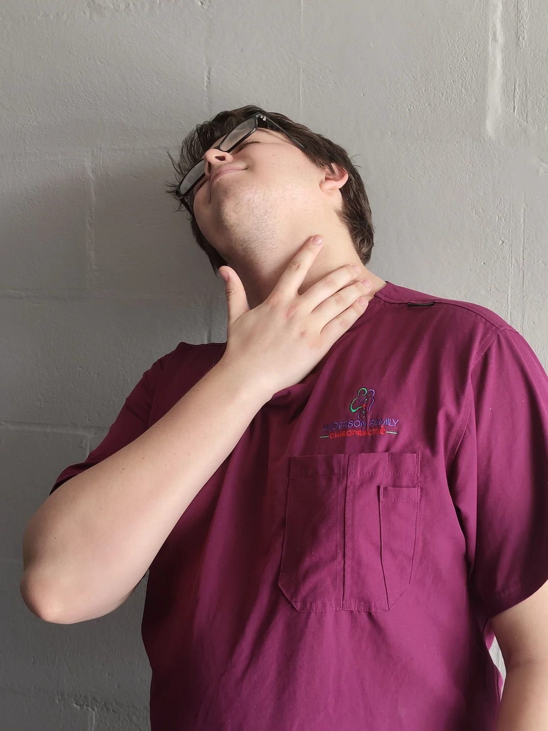 A Man Wearing a Purple Shirt Has His Hand on His Neck — Anderson Family Chiropractic Health Centre in Mount Pleasant, QLD
