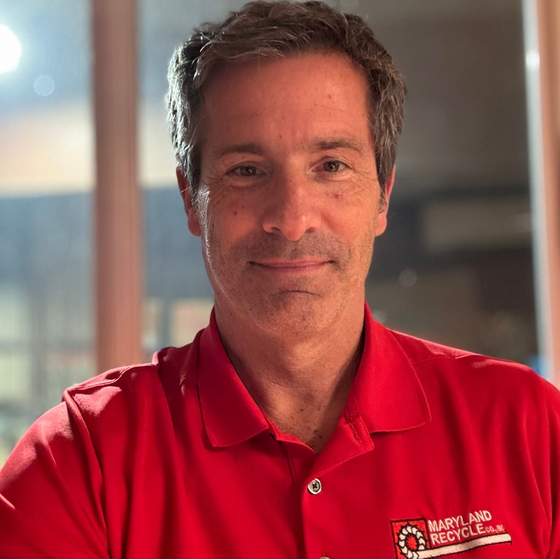 A smiling family of four poses together outdoors with the ocean in the background.