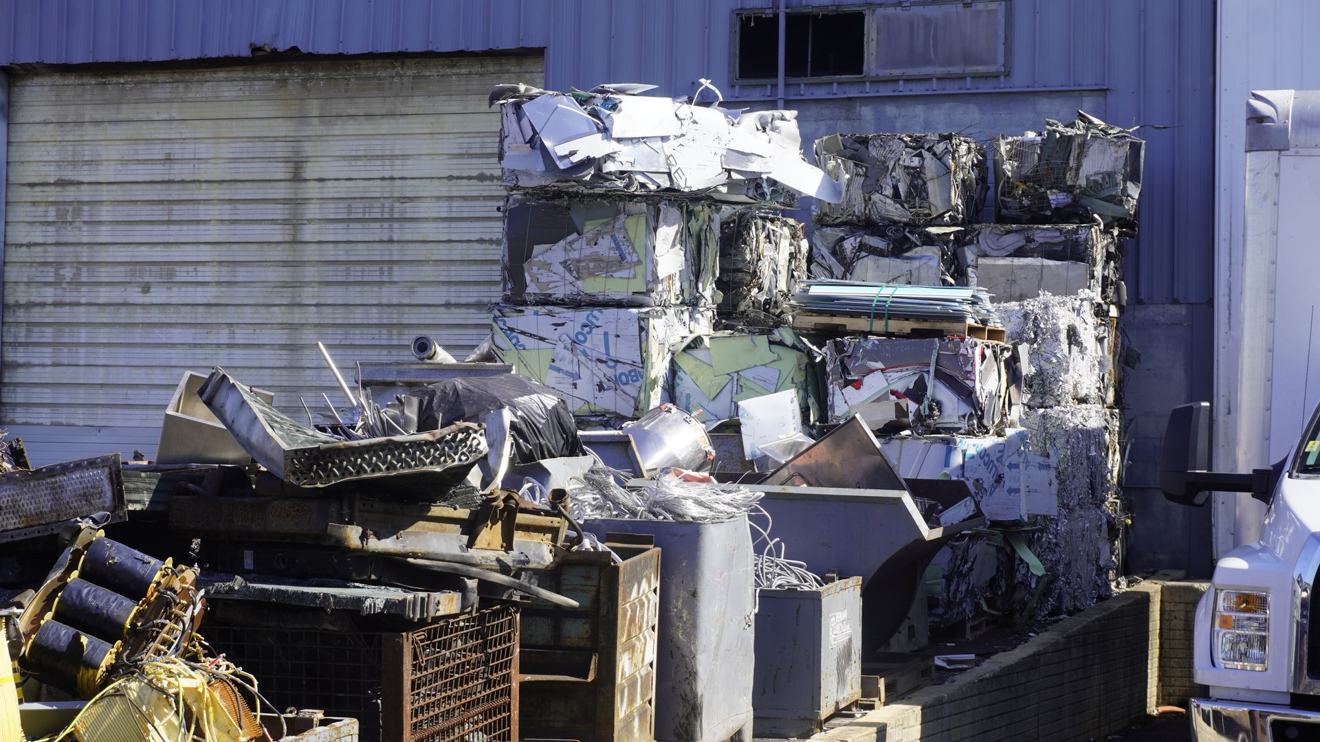Damaged industrial machine and debris beside a warehouse wall, with a white truck at right.