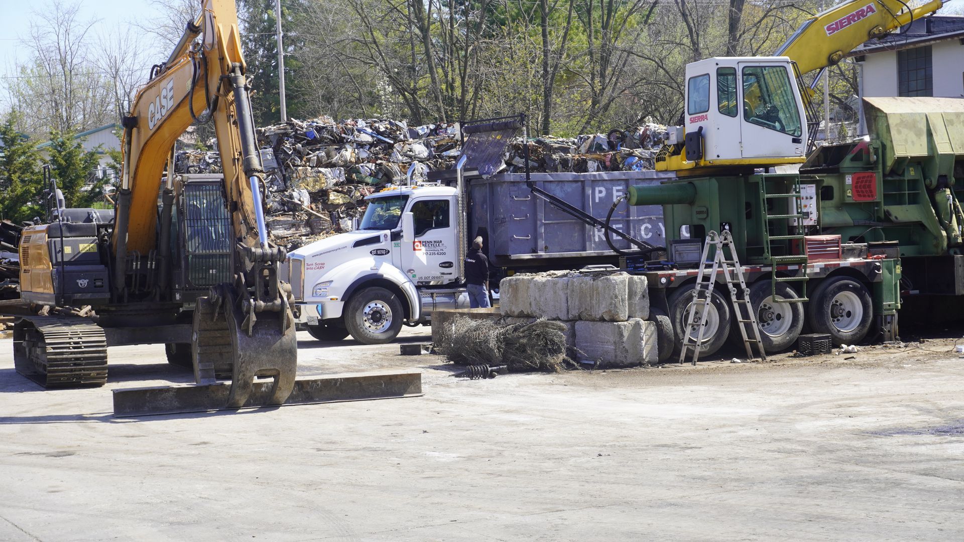 Construction vehicles parked in a lot, including excavators, a truck, and a large machine with cables.