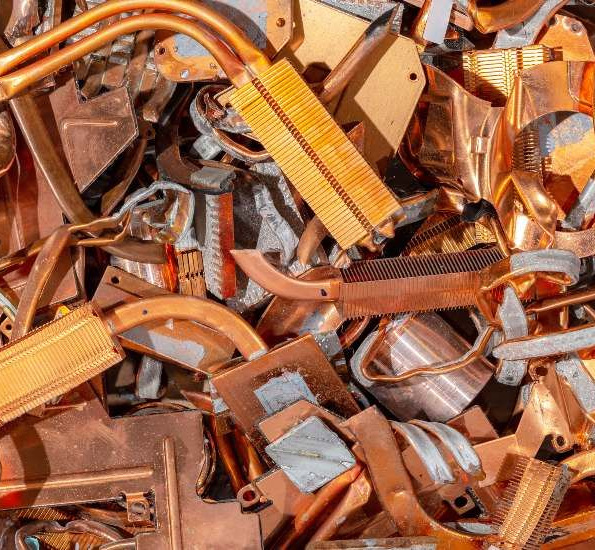 Pile of shiny copper and aluminum scrap metal pieces, mixed orange, silver, and brown tones.