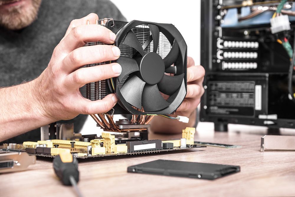 A Man is Fixing a Computer With a Fan in His Hands — Complete Computing Consultancy In Maryborough, QLD