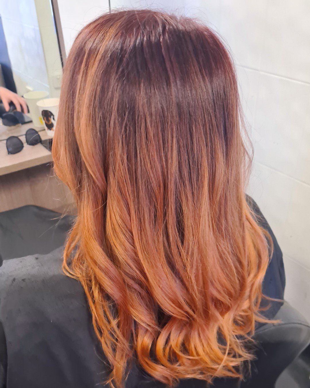 A back view of medium-length, wavy, dark to vibrant red orange ombre hair.