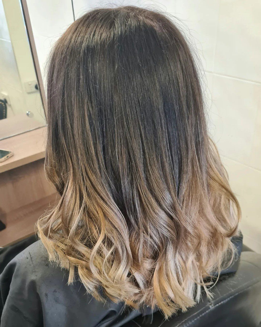 A woman with ombre hair is sitting in a chair in front of a mirror.