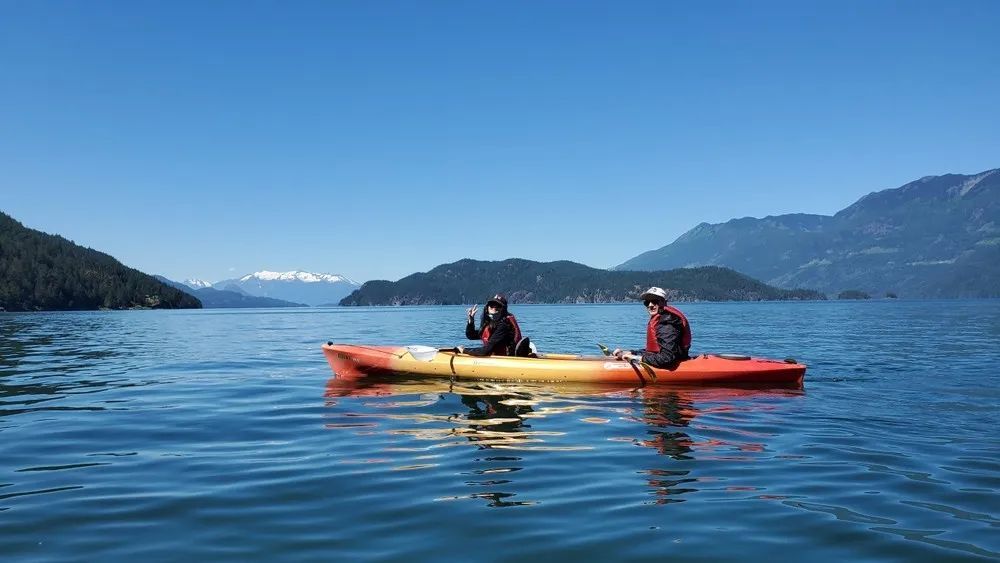 Two people in kayaks on a lake with mountains in the background