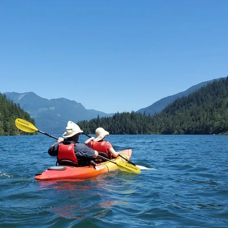 Two people in kayaks on a lake with mountains in the background