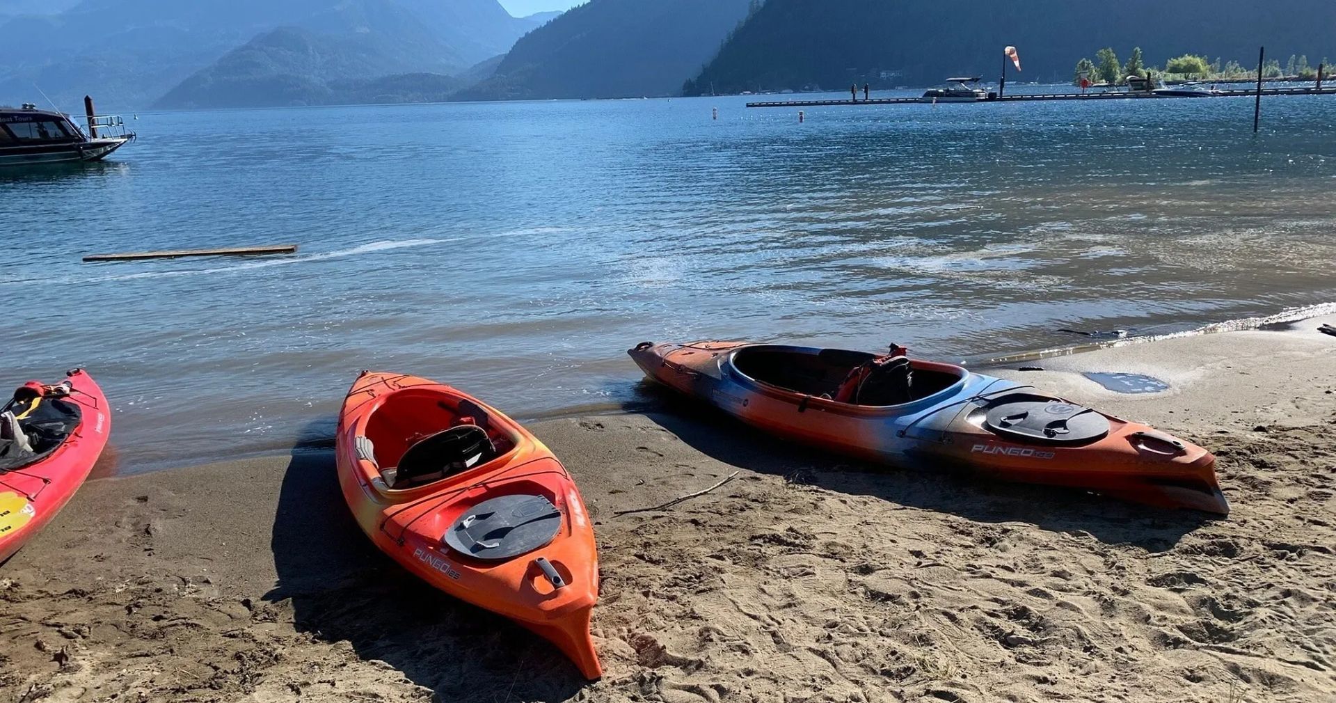 Three kayaks are on a sandy beach near the water