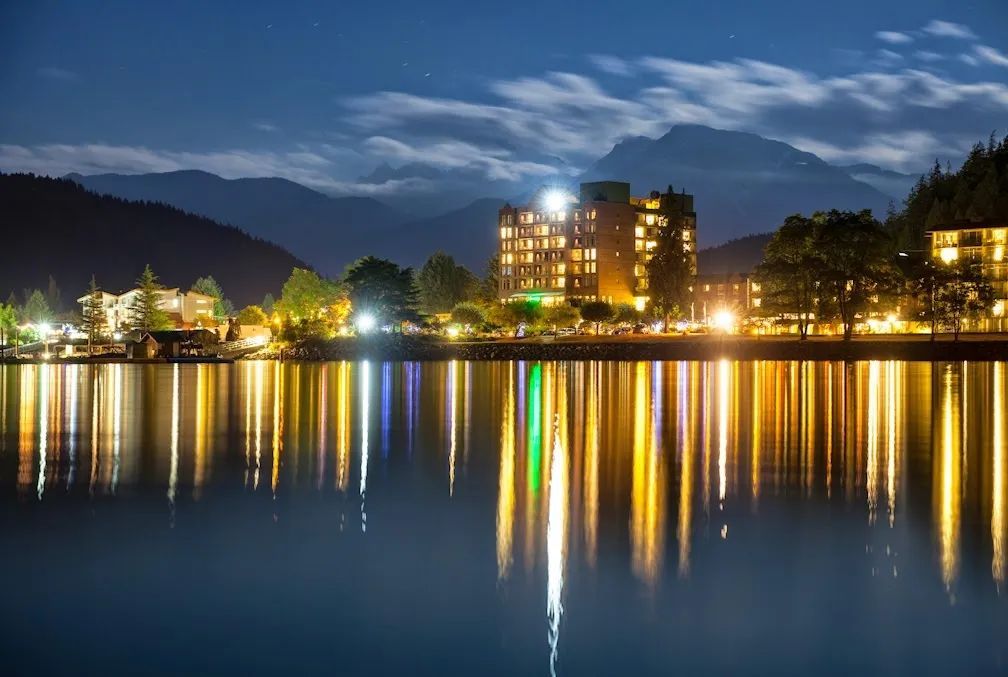 A large building sits on the shore of a lake at night