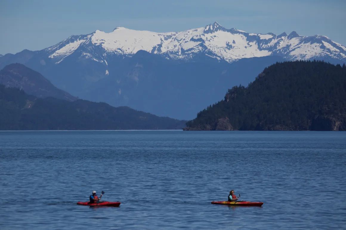 Two people in kayaks in a lake with mountains in the background