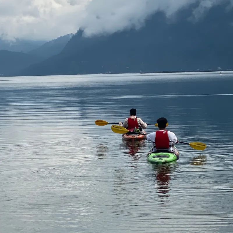 Two people in kayaks on a lake with mountains in the background