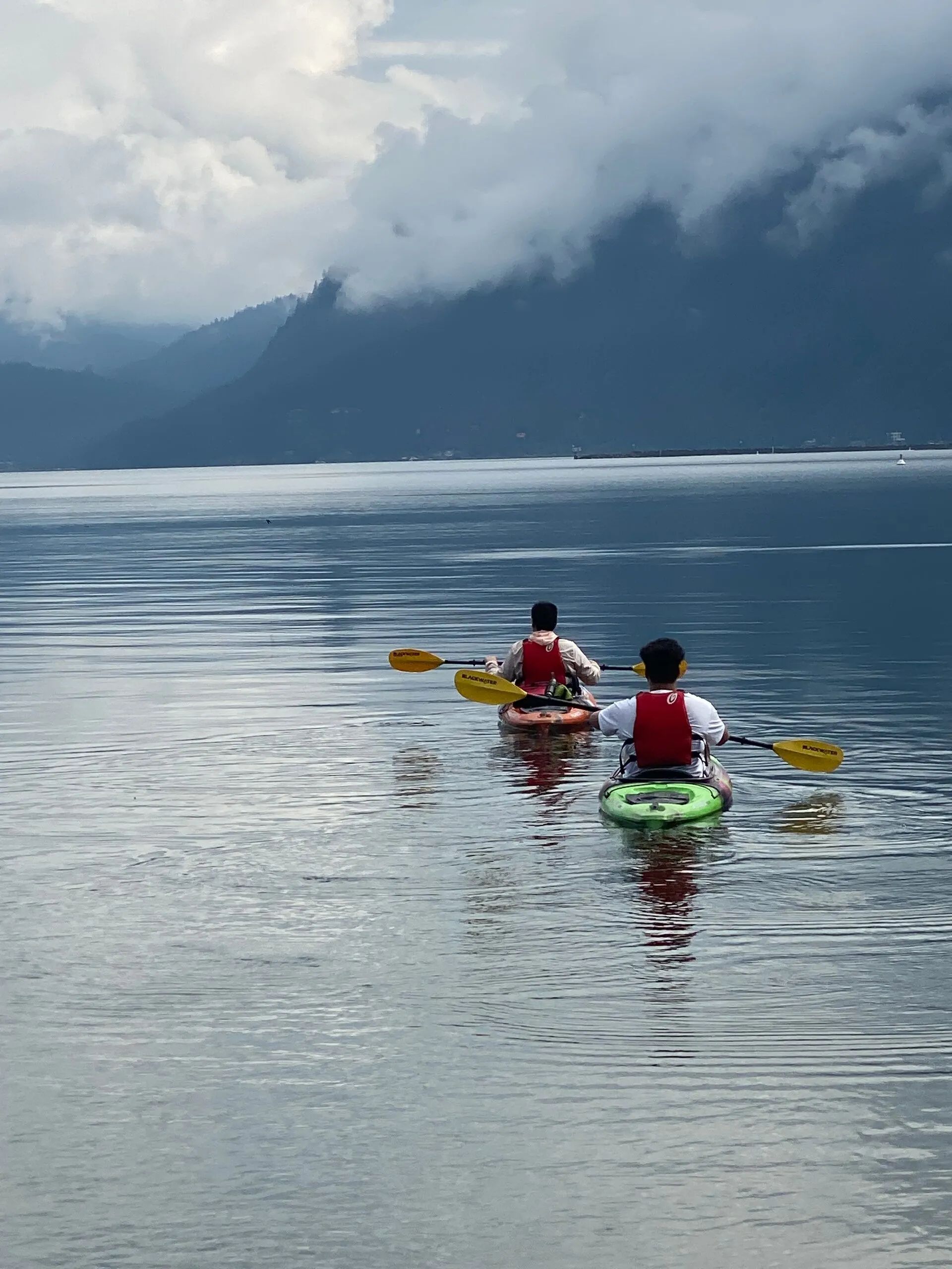 Two people in kayaks on a lake with mountains in the background