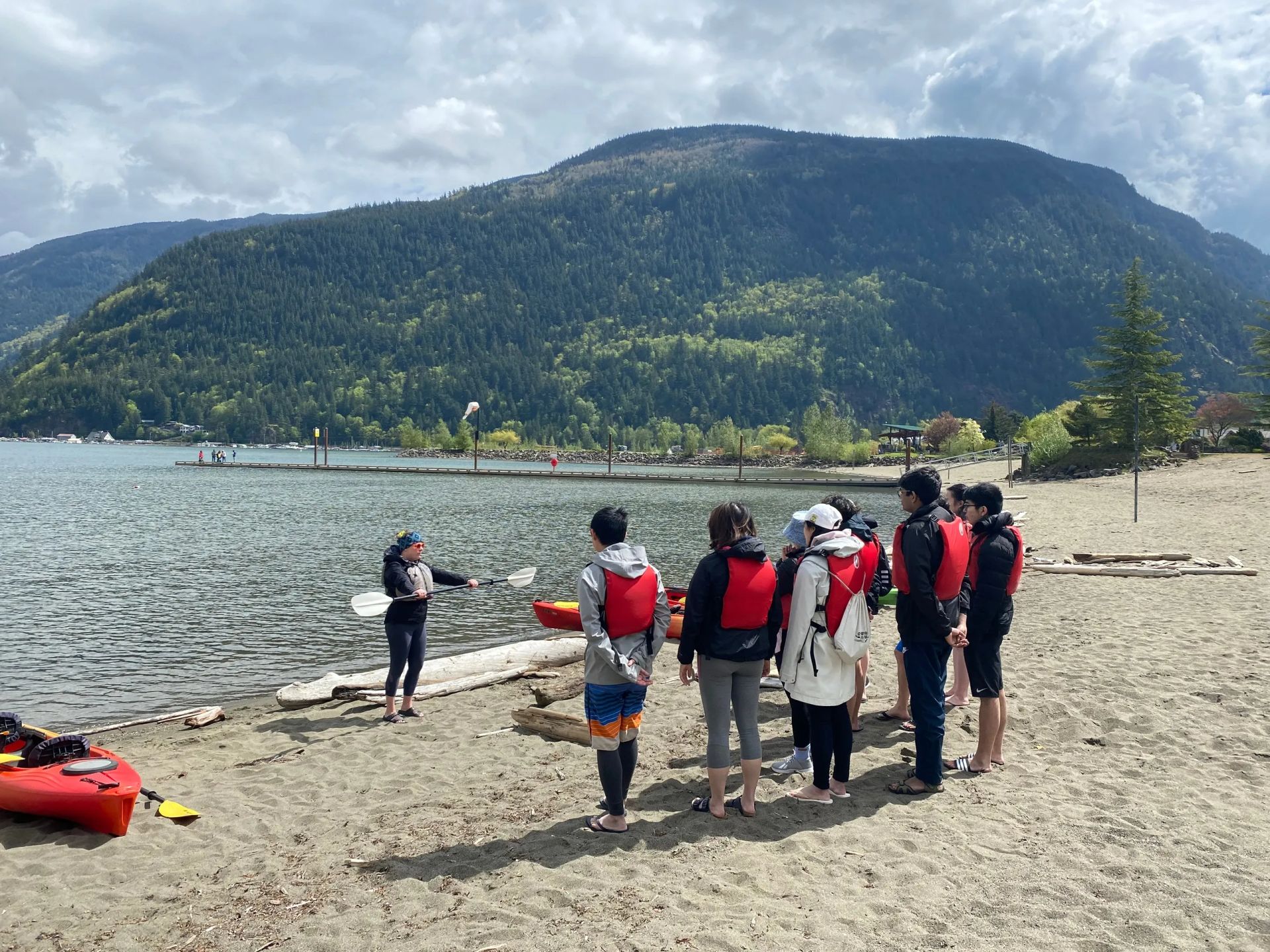 A group of people standing on a beach with mountains in the background