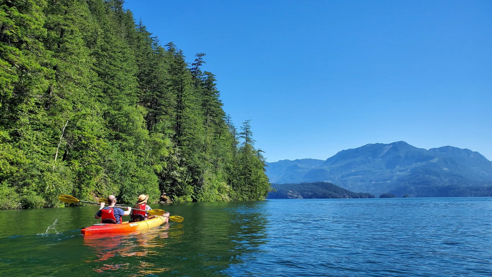 Two people in a kayak on a lake with mountains in the background