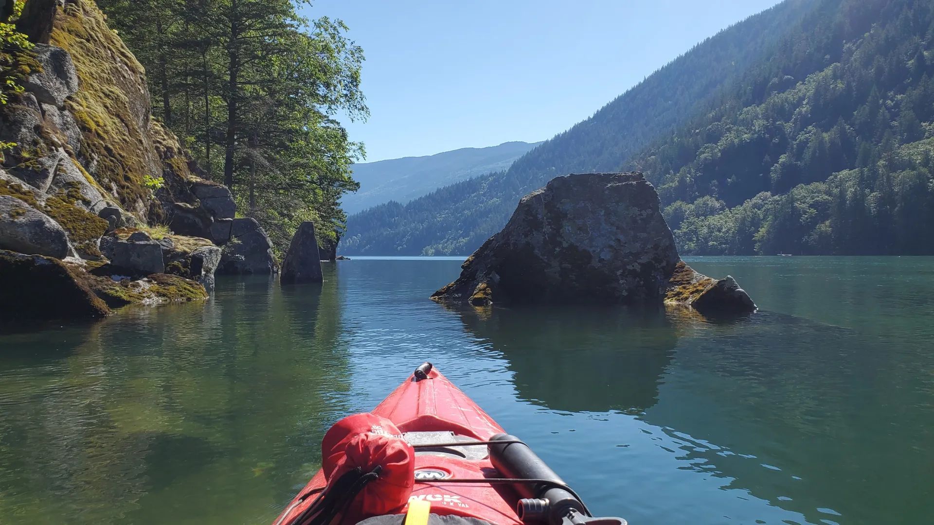 A red kayak is floating on a lake with mountains in the background
