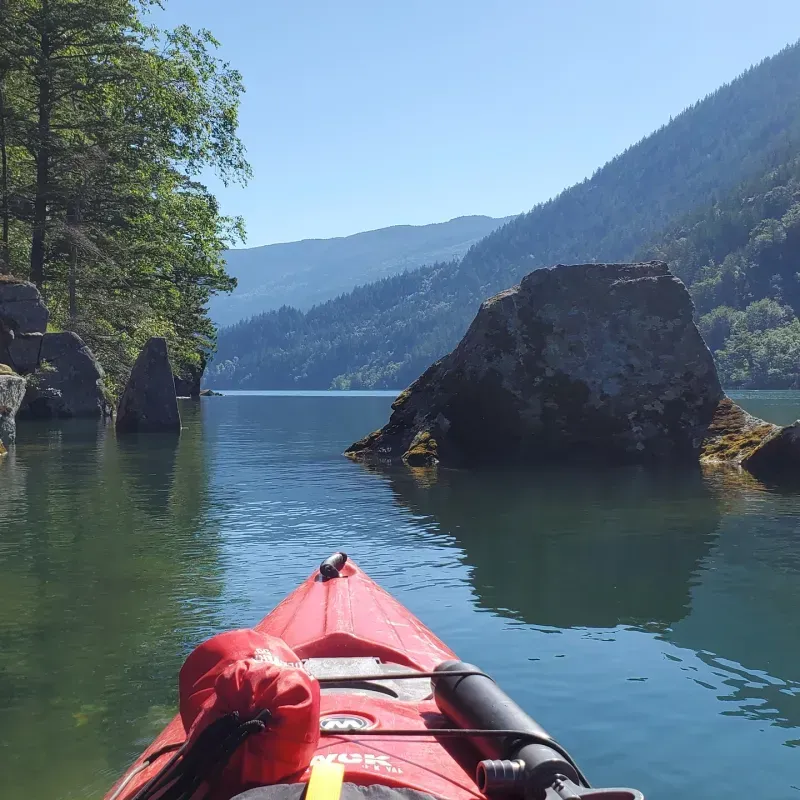A person in a red kayak on a lake with mountains in the background