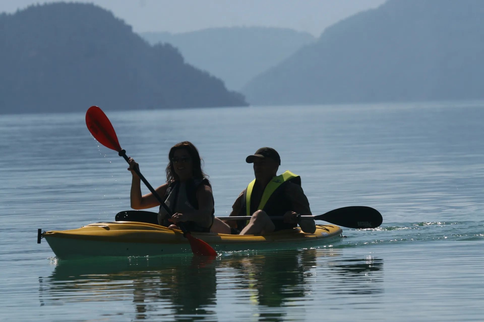 A man and a woman are paddling kayaks on a lake