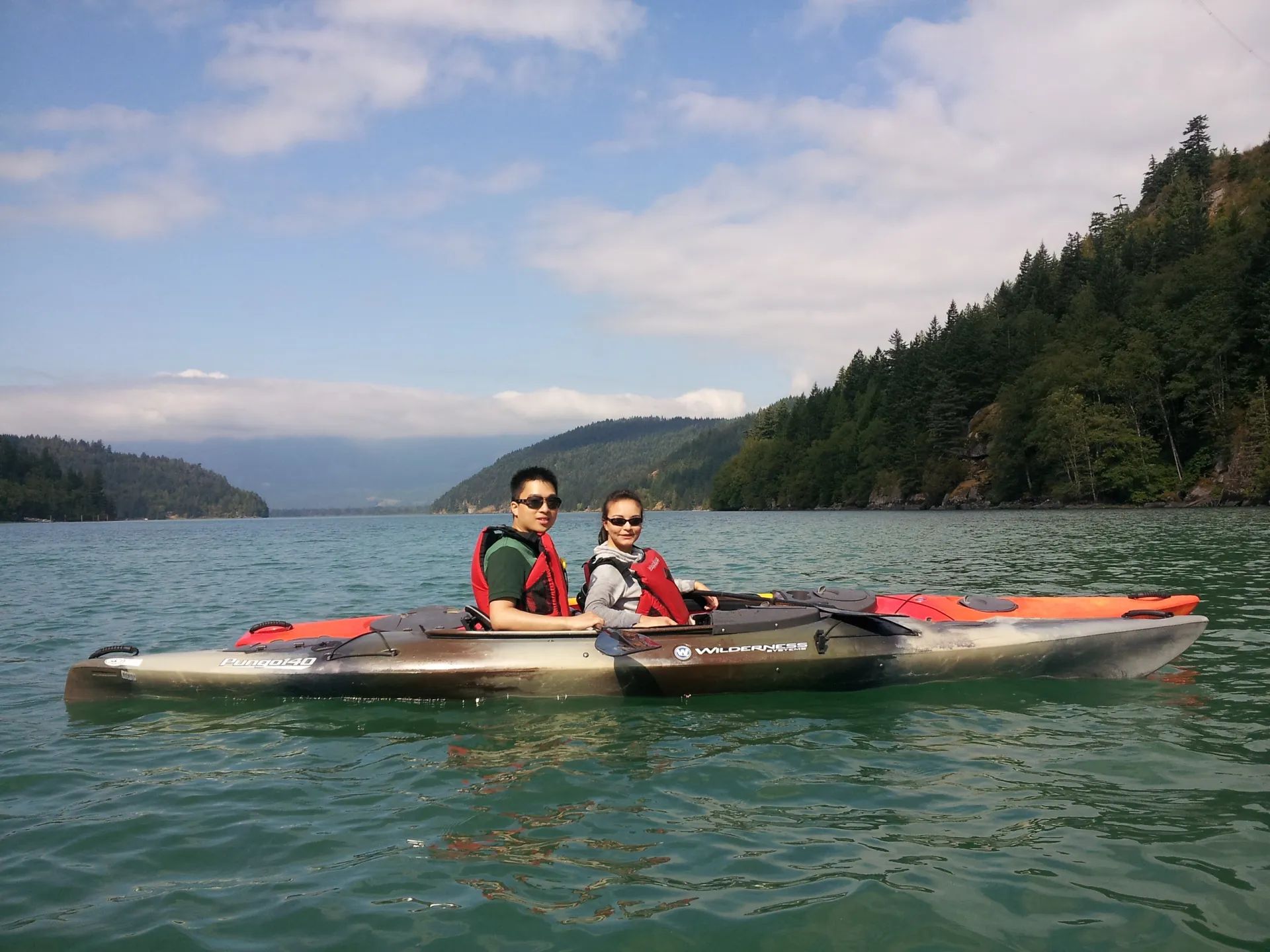 Two people in a kayak on a lake with mountains in the background