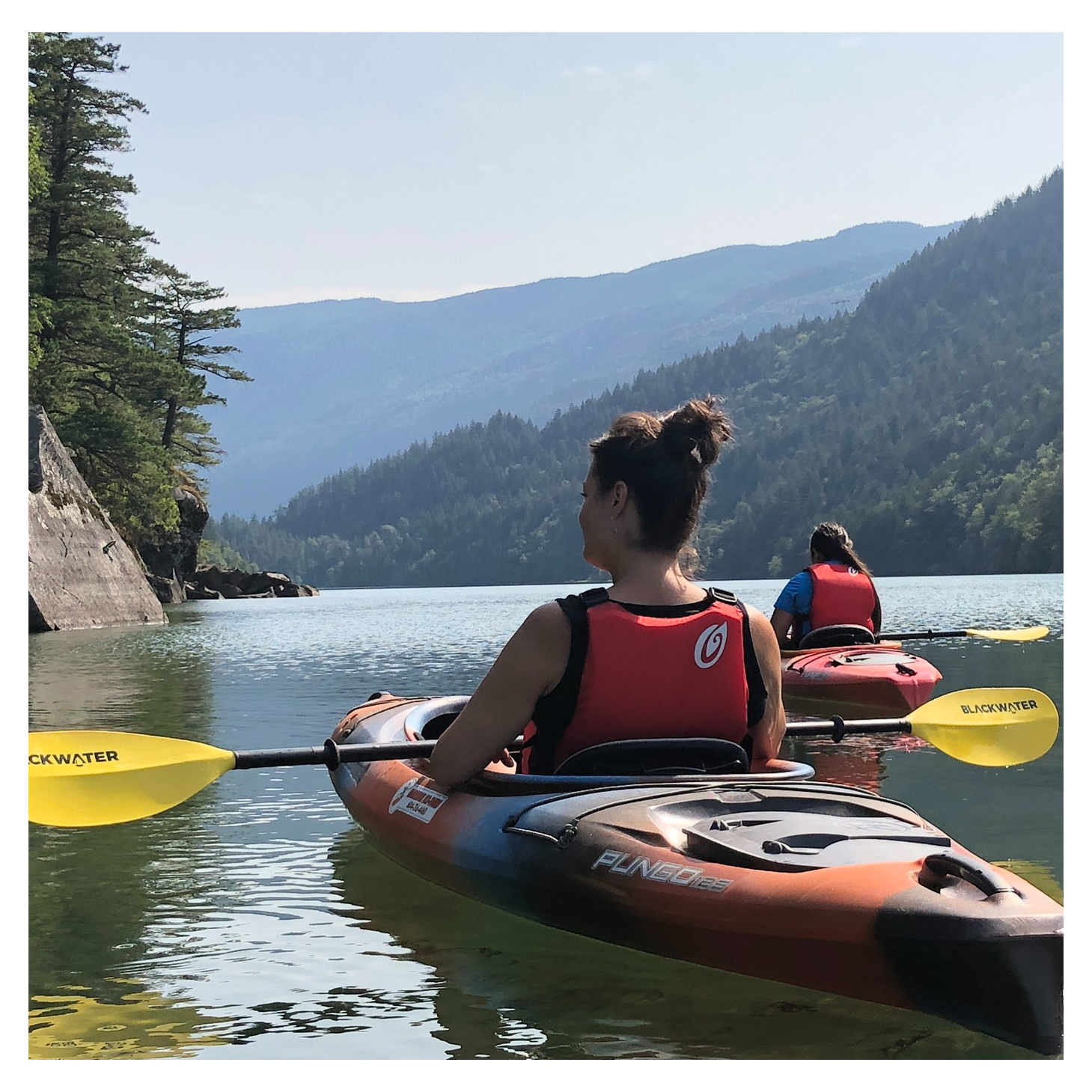 A woman in a red vest is paddling a kayak on a lake