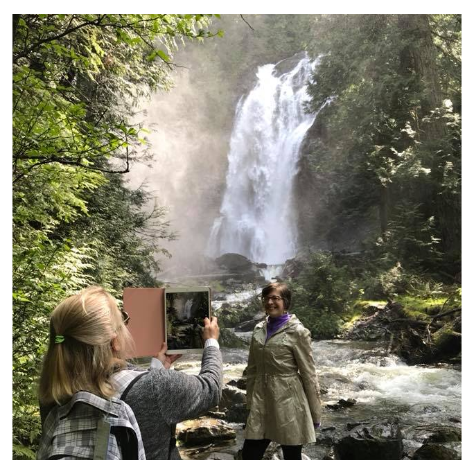 A woman is taking a picture of a waterfall with her phone.