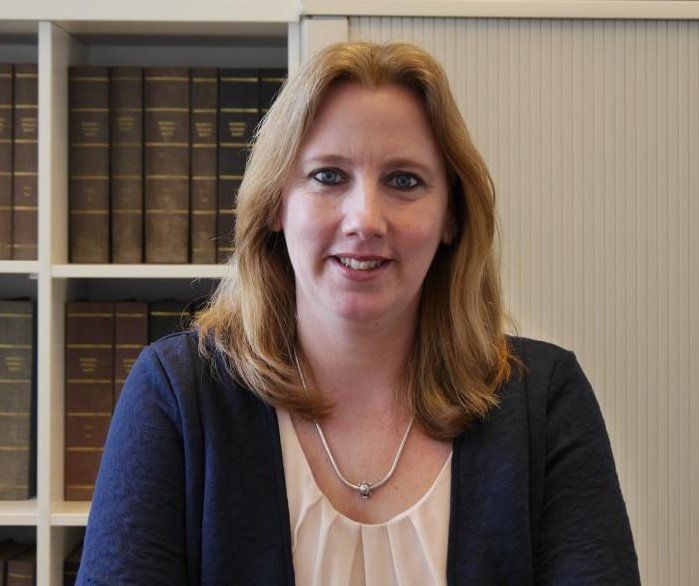 Eine Frau sitzt vor einem Bücherregal und lächelt