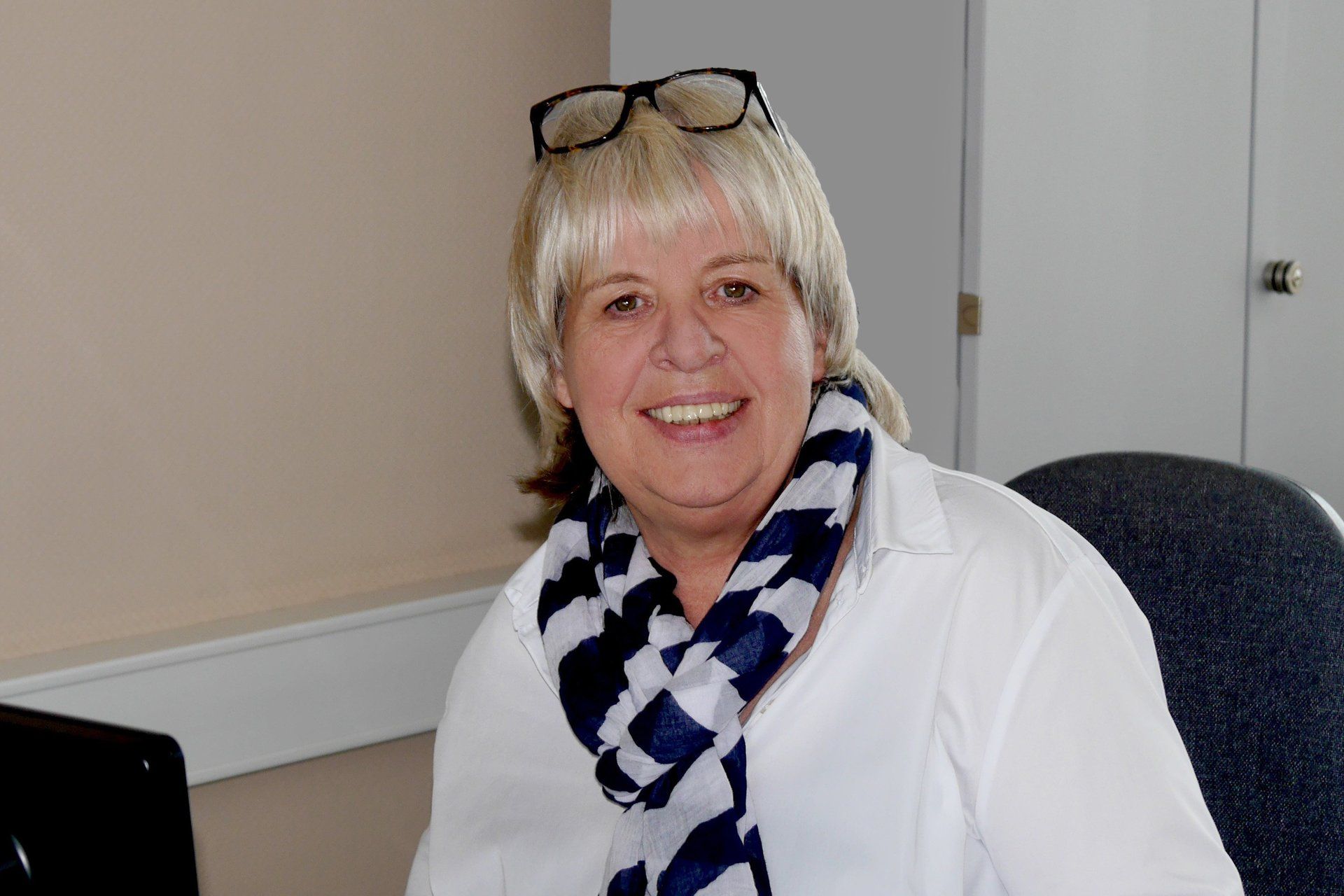 Eine Frau mit Brille und Kopftuch sitzt auf einem Stuhl.