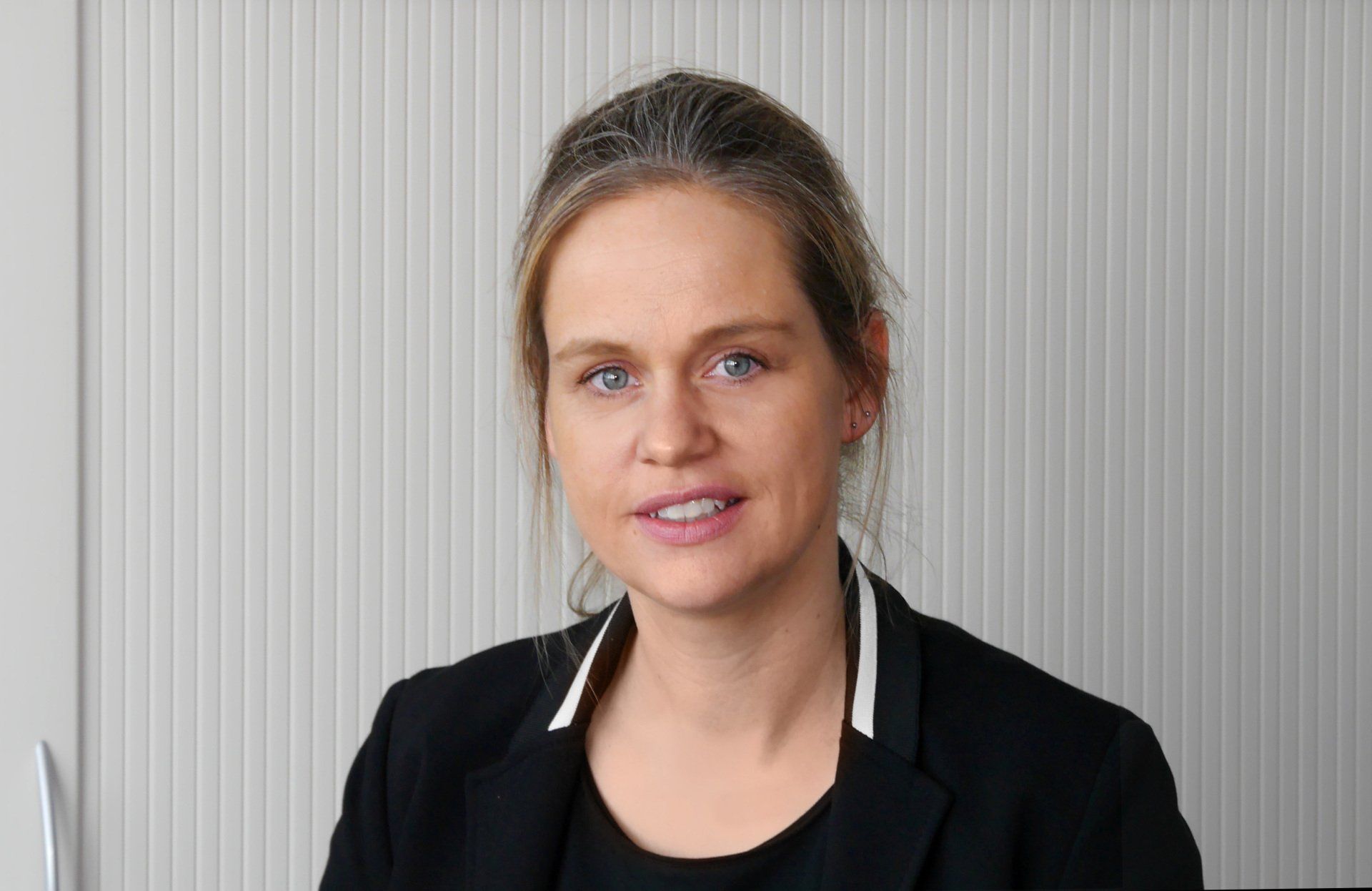 Eine Frau in einer schwarzen Jacke lächelt in die Kamera.