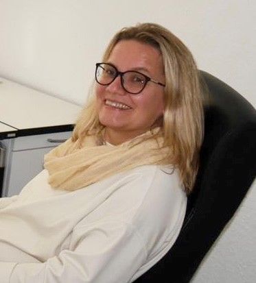 Eine Frau mit Brille und Kopftuch sitzt auf einem Bürostuhl.