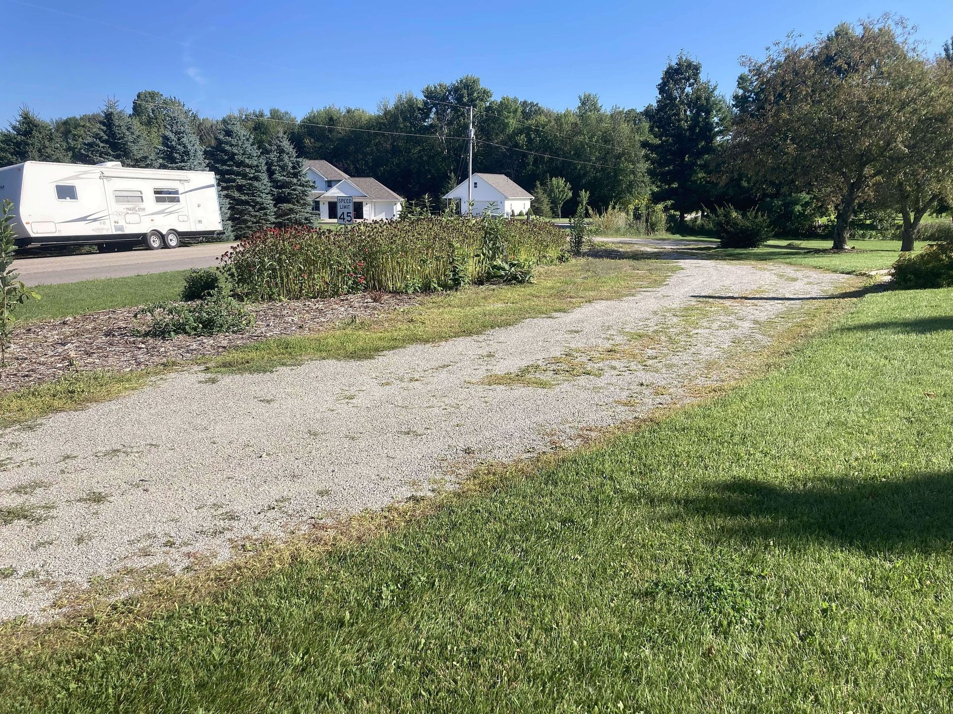 A rv is parked on the side of the road next to a gravel path.