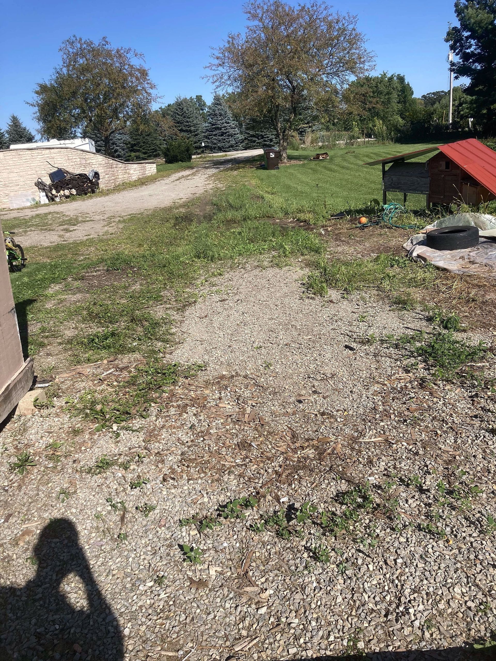 A gravel road going through a grassy field with a red roof.
