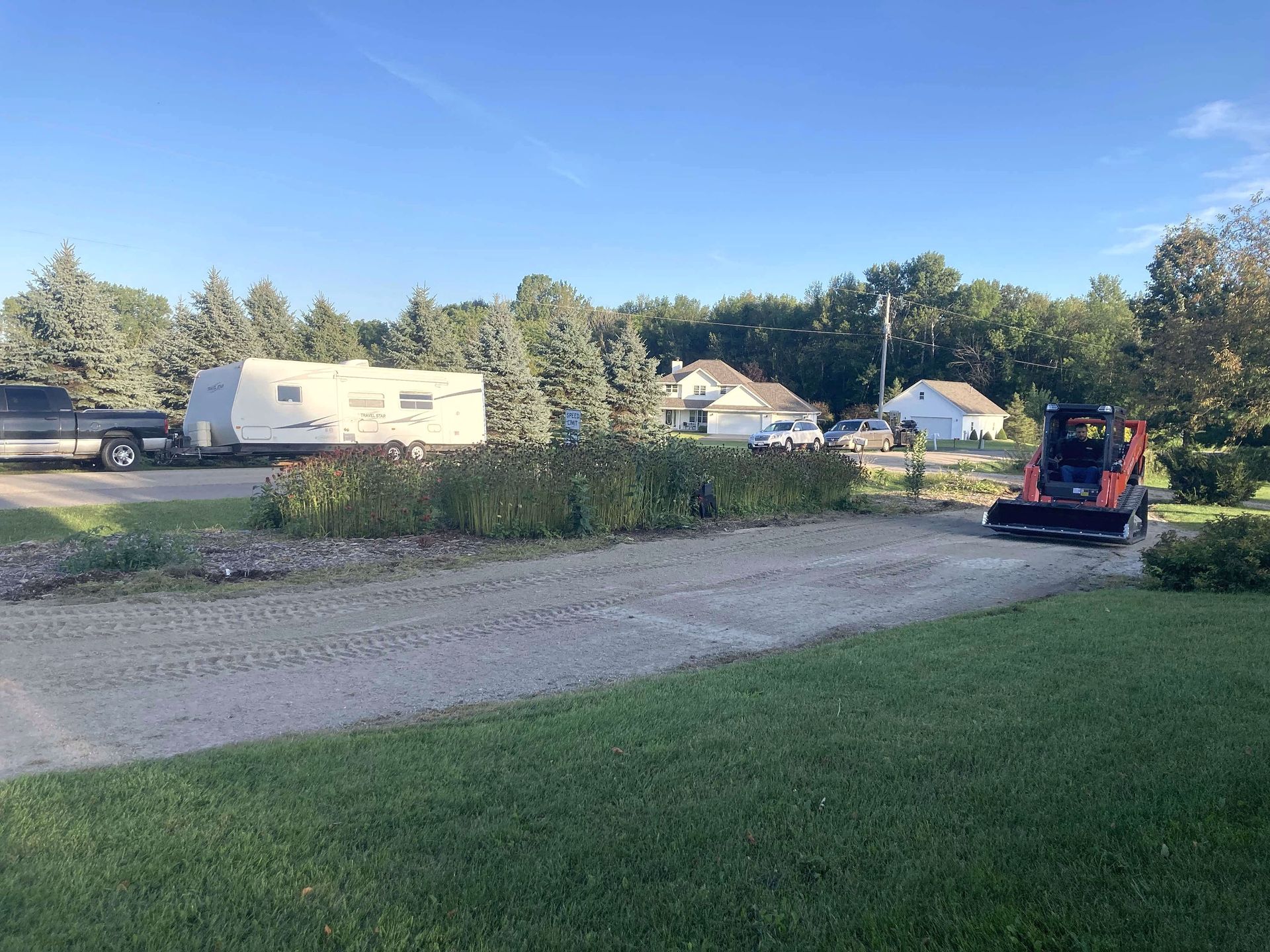 A tractor is driving down a dirt road next to a trailer.