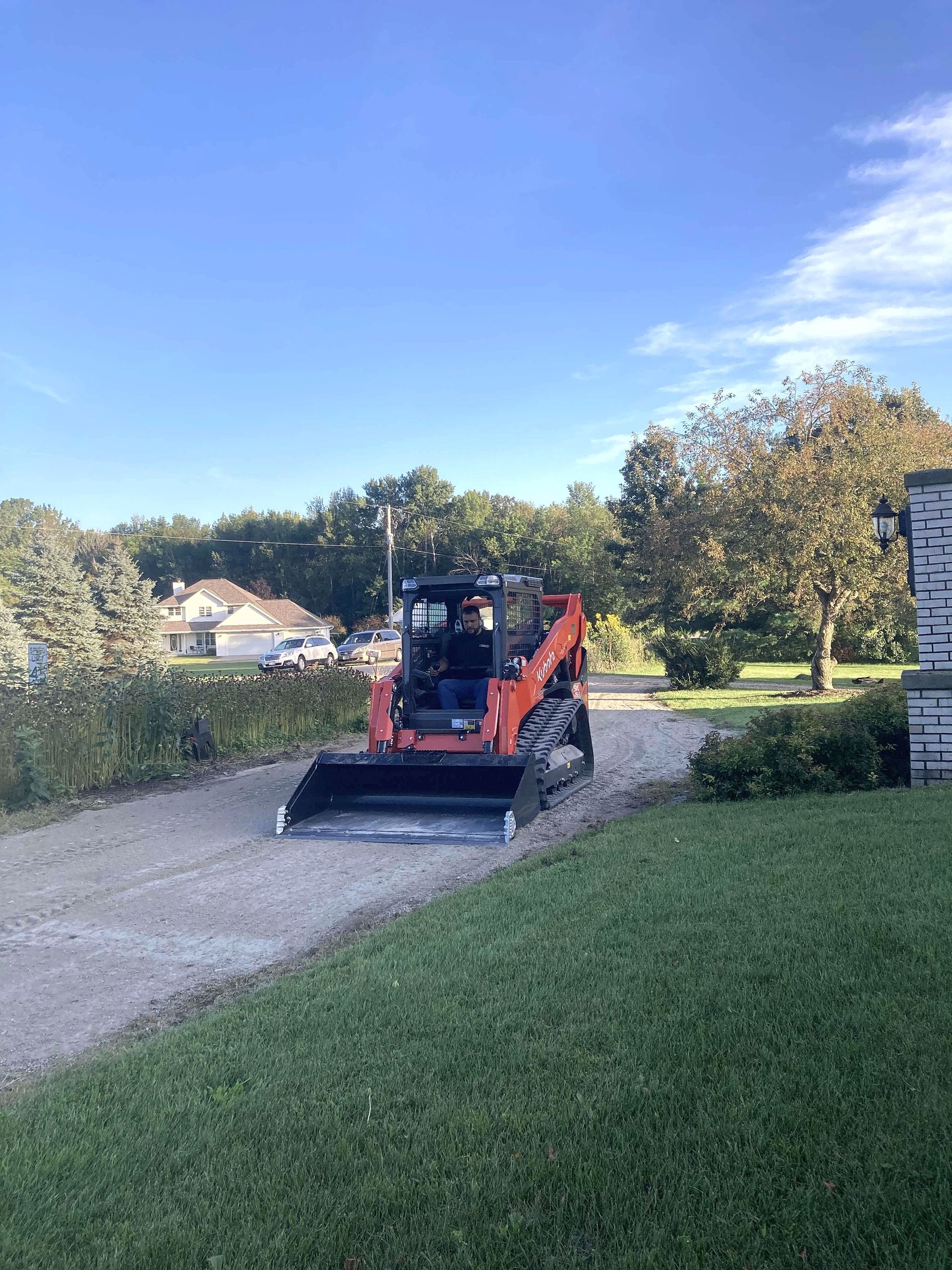 A bulldozer is driving down a dirt road next to a house.