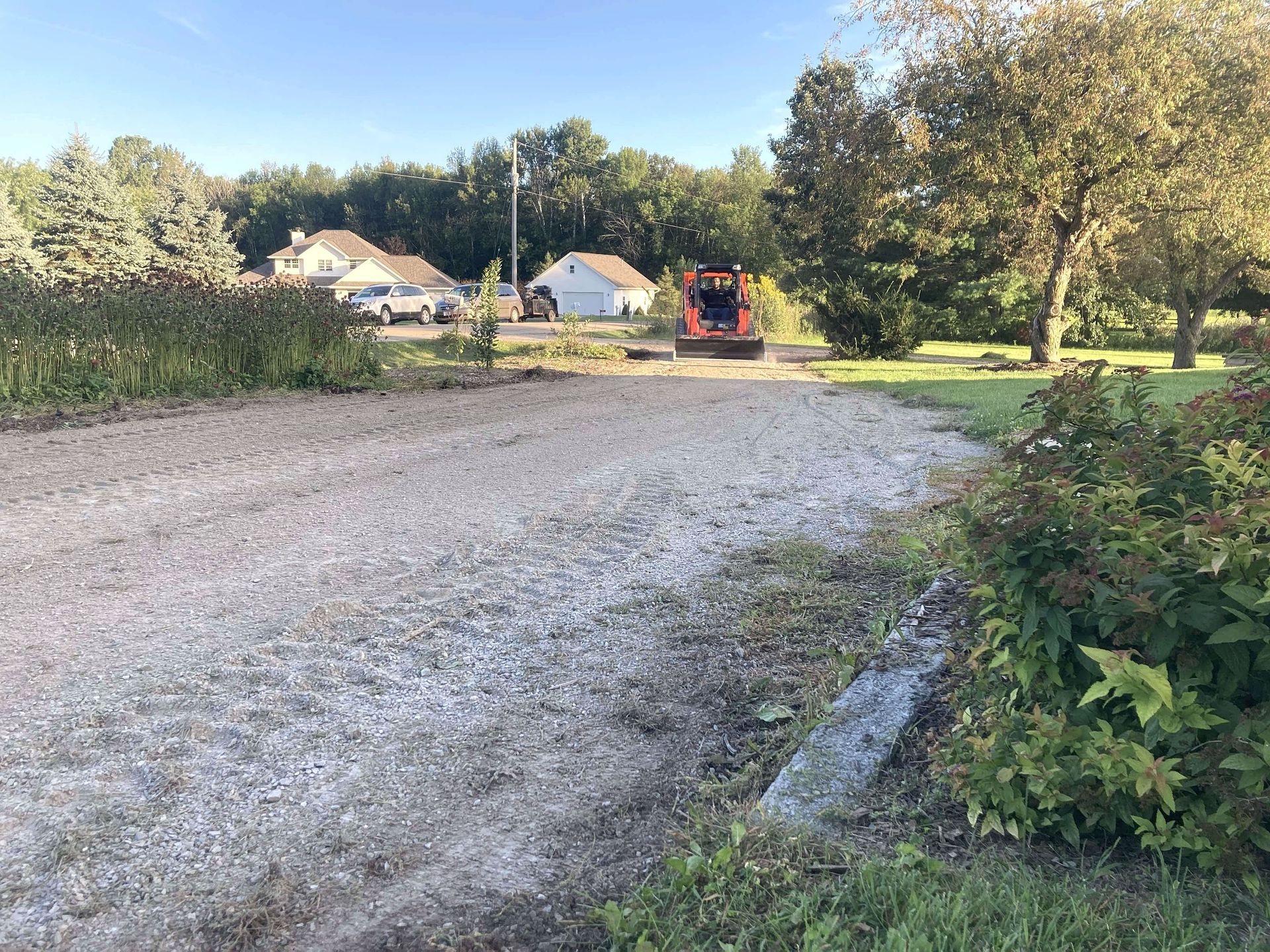 A gravel driveway leading to a house with a tractor in the background.