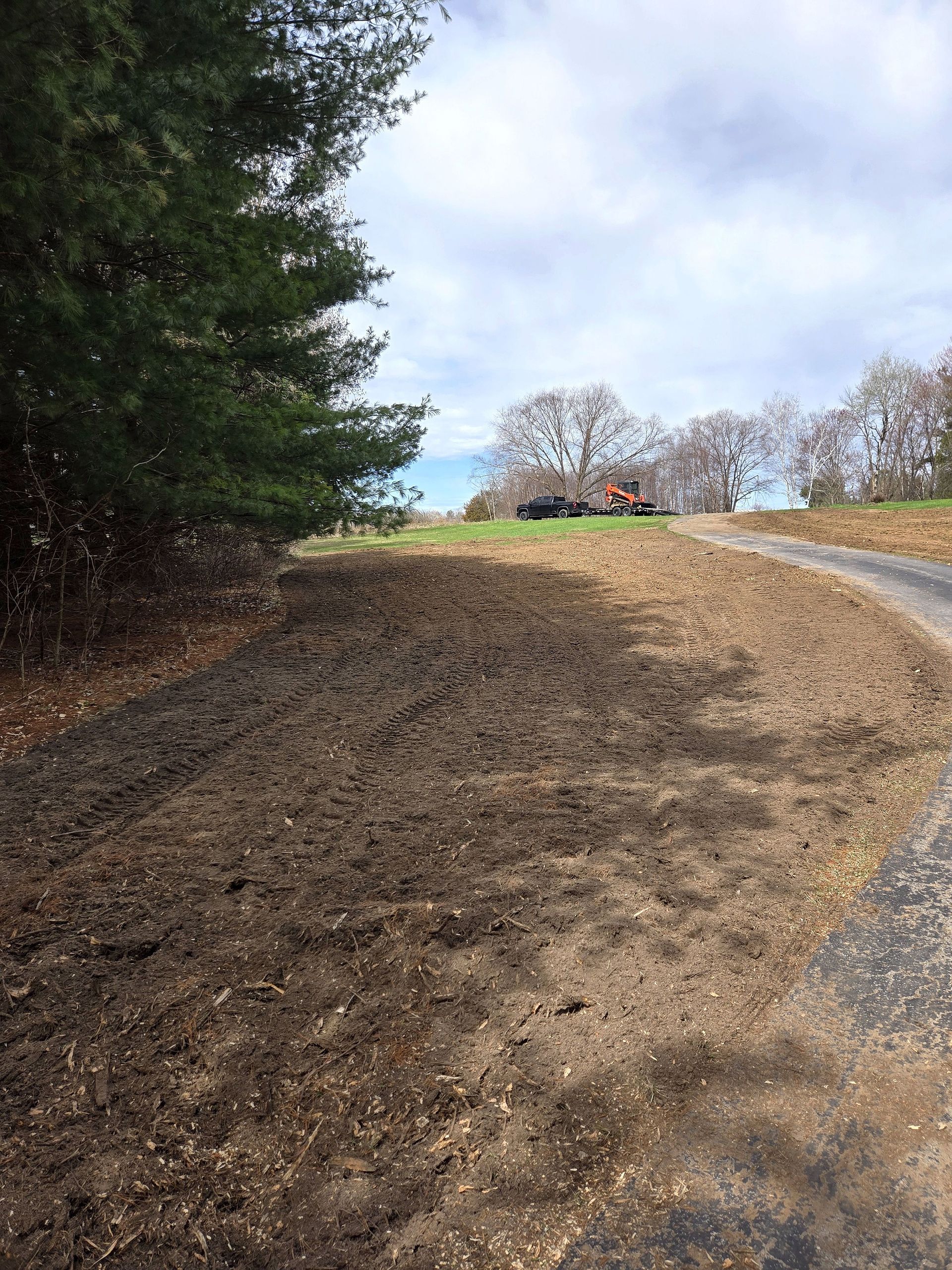 A dirt road going through a field with a house in the background.