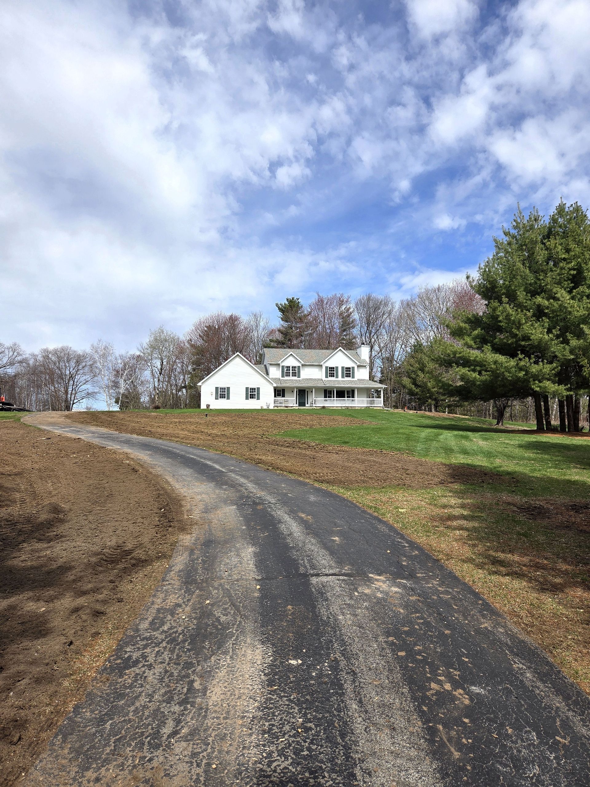 A large white house is sitting on top of a hill next to a dirt road.