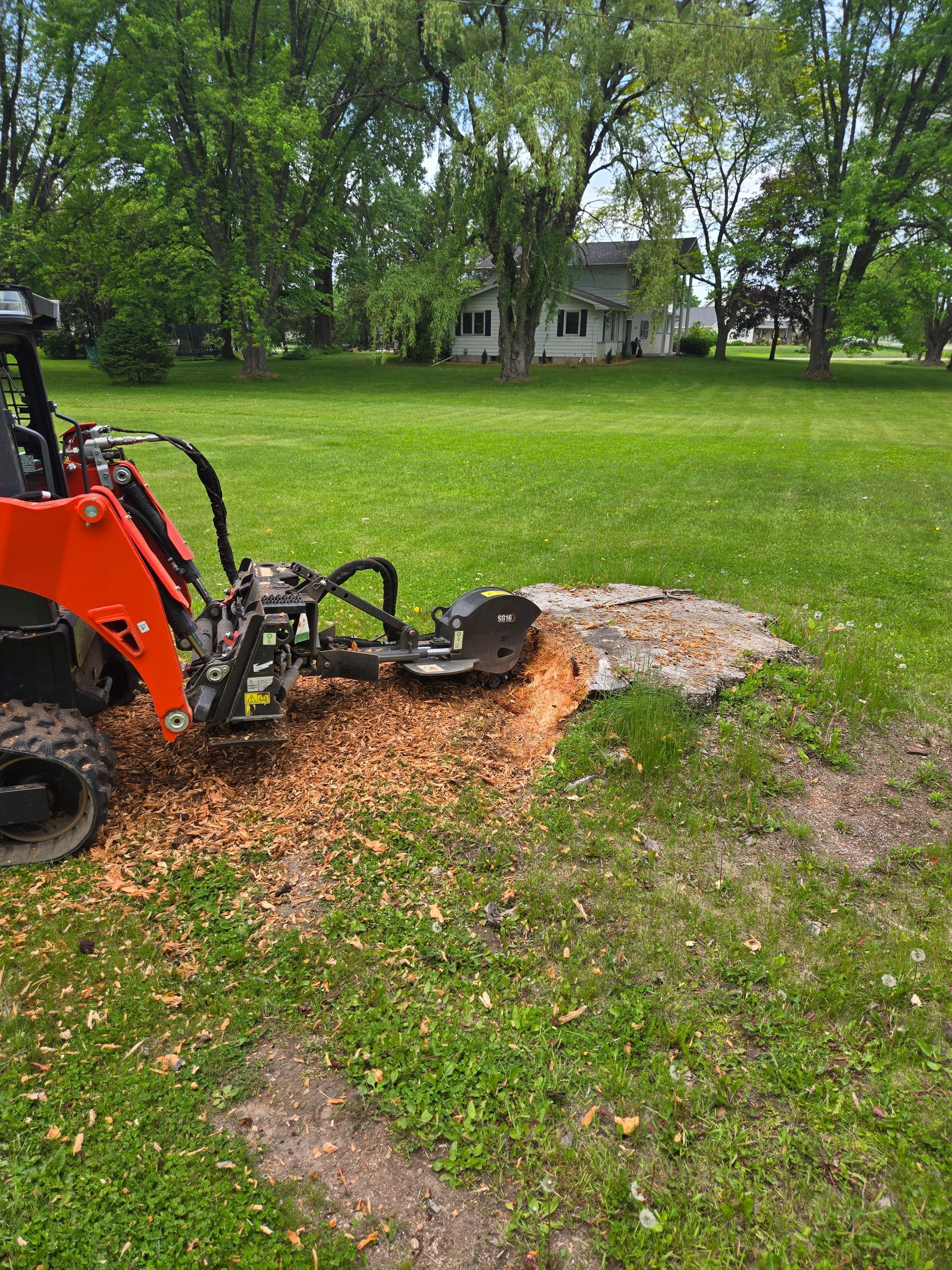 A tractor is stump grinding a tree stump in a grassy field.