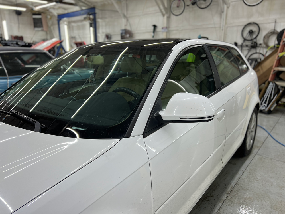 A white car with a black roof is parked in a garage.