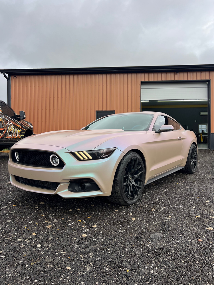 A pink ford mustang is parked in front of a building.