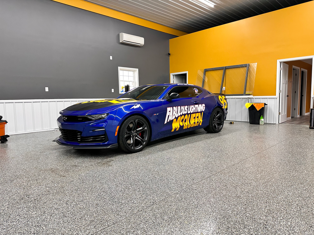 A blue car is parked in a garage with a yellow wall.