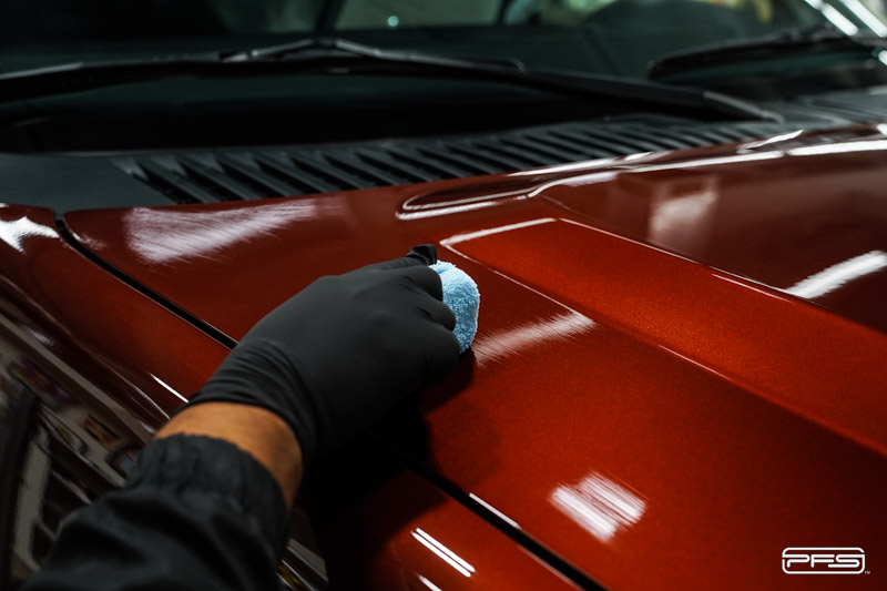 A person wearing black gloves is polishing the hood of a red car.