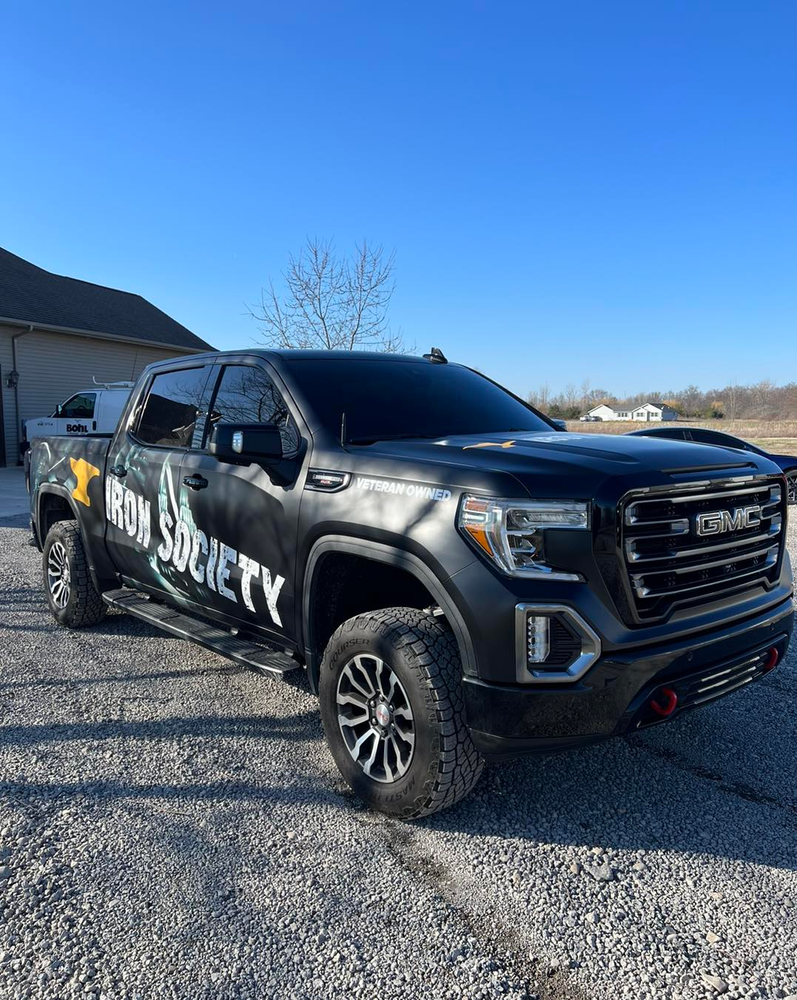 A black truck is parked in a gravel lot in front of a house.