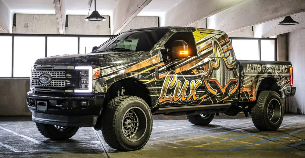 A black truck with graffiti on the side is parked in a parking garage.