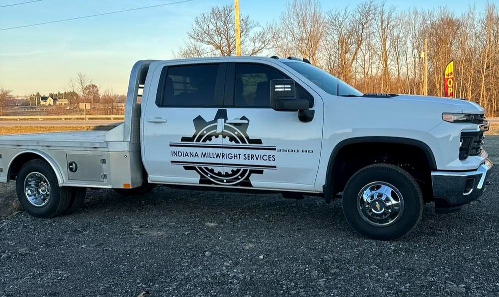 A white truck with a flat bed is parked in a gravel lot.