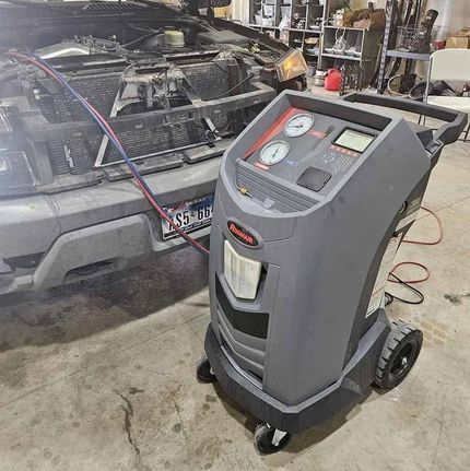 An automotive A/C refrigerant recovery and recharge machine connected to a car in a repair shop.