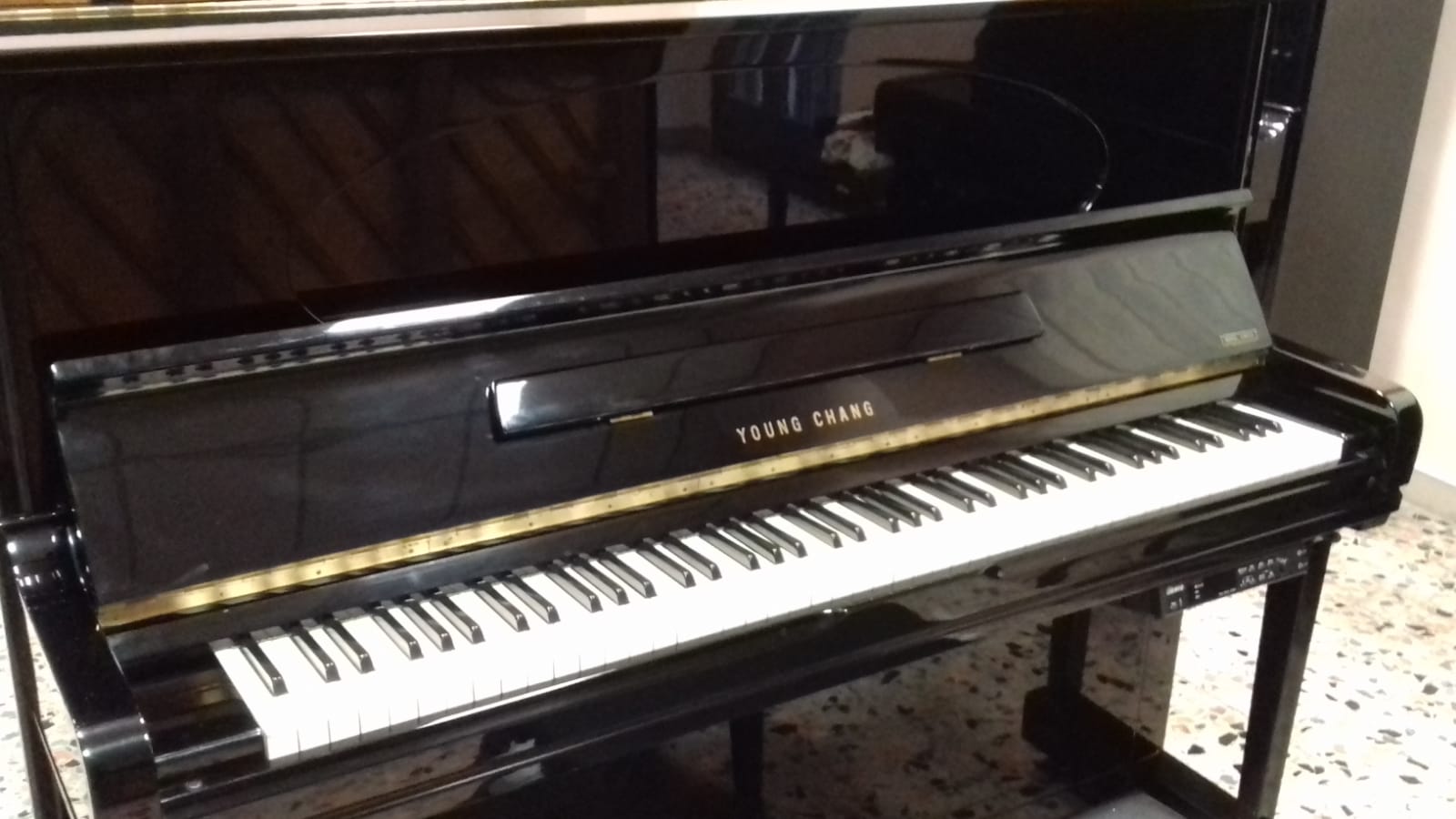 Un pianoforte verticale nero è appoggiato su un pavimento piastrellato
